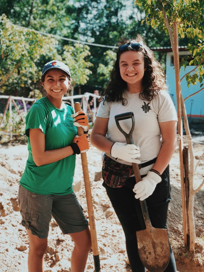 Two volunteers standing with shovels beside a newly planted tree.