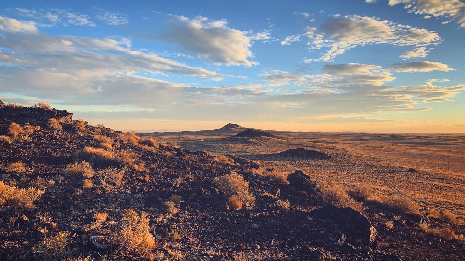 High desert plain outside Albuquerque at sunset, with volcanic rock in the foreground and a mesa on the horizon.